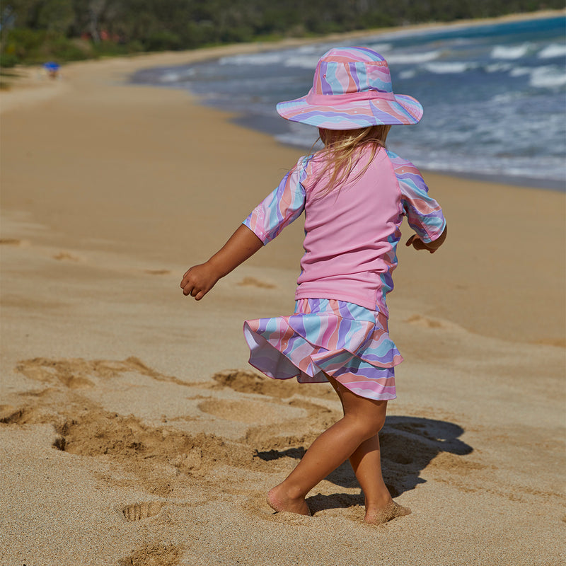 Little girl running on the beach in UV Skinz's girl's short sleeve sunny swim shirt in rollin along|rollin-along