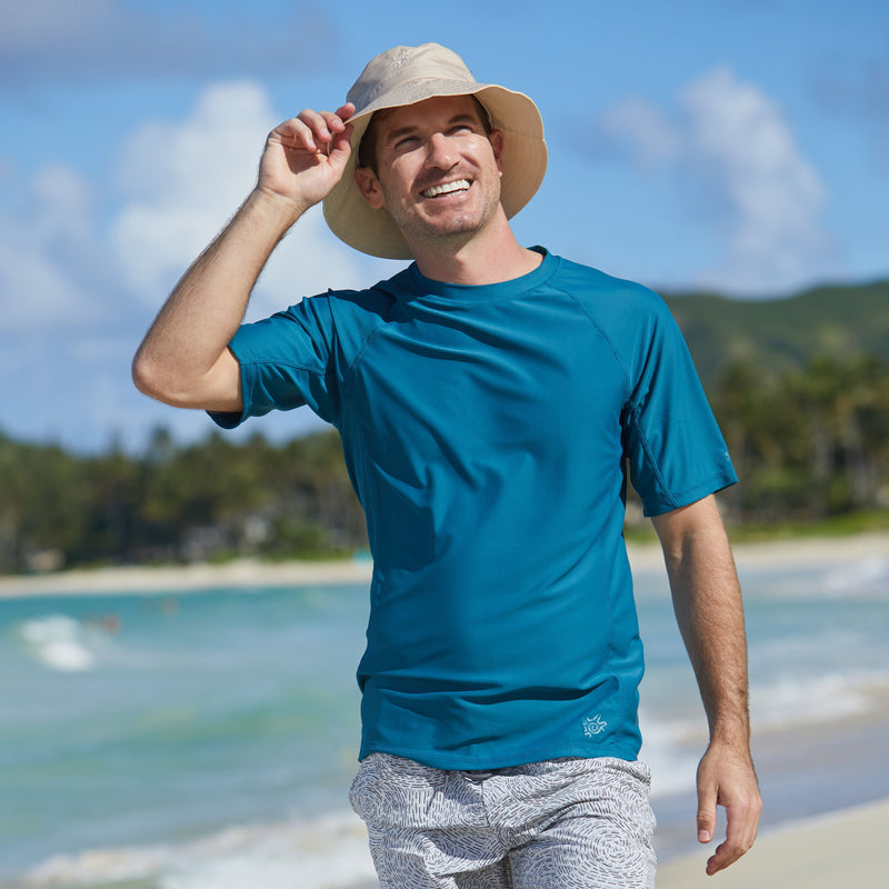 Man walking on the beach in UV Skinz's men's short sleeve swim shirt in dark teal|dark-teal