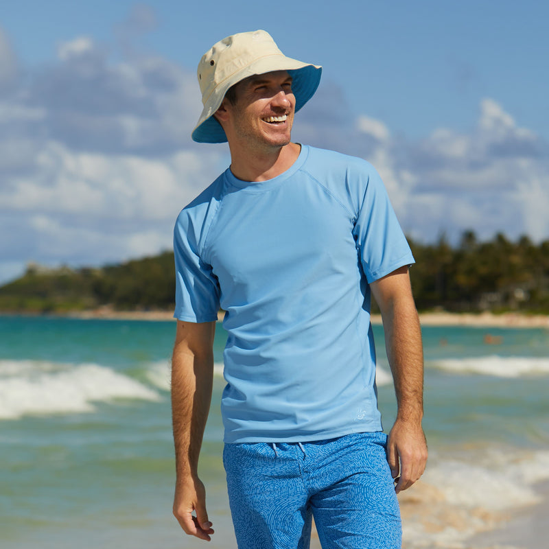Man on the beach in UV Skinz's men's short sleeve swim shirt in light blue|light-blue