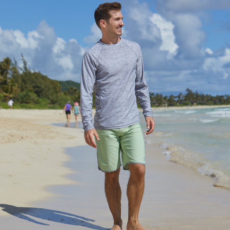 Man on the beach in UV Skinz's men's board shorts in electric green zigzag|electric-green-zigzag