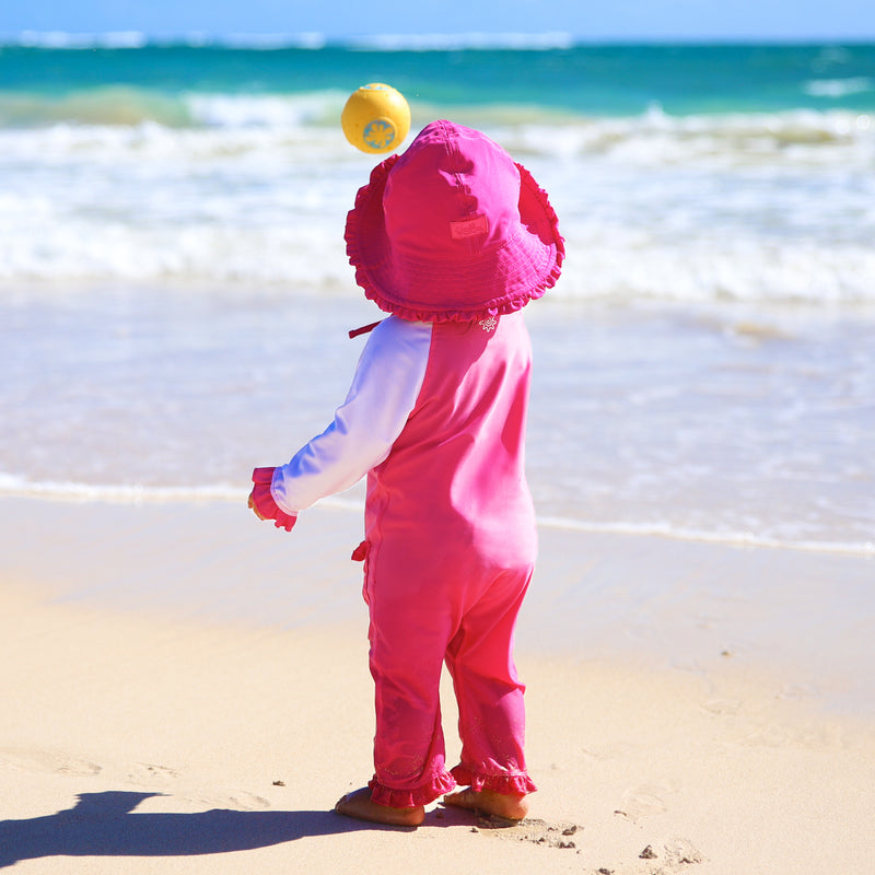 Baby girl in UV Skinz's baby girls long-sleeve swimsuit in bubblegum white on the beach|bubblegum-white