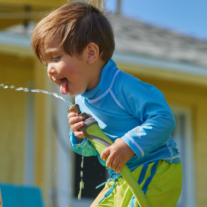 Baby boy playing with a hose in UV Skinz's baby long sleeve swim shirt in ocean blue|ocean-blue